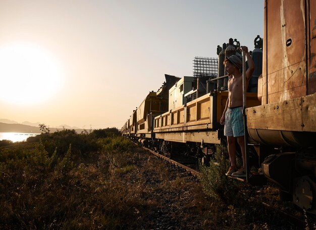 Jeune homme debout dans un train au coucher du soleil, prêt pour l'aventure