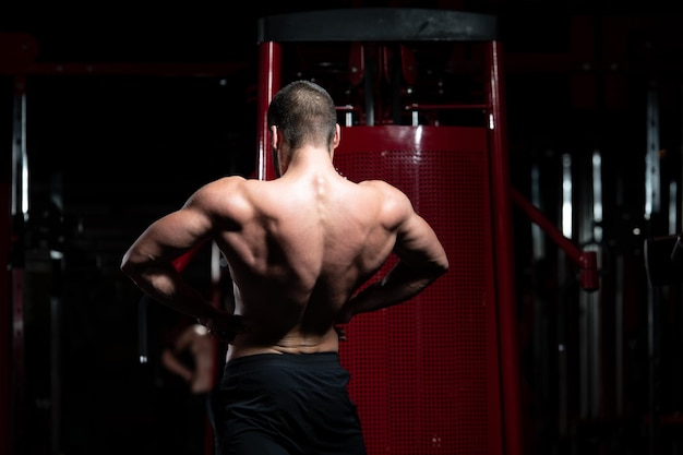 Jeune homme debout fort dans la salle de gym et muscles fléchissants - modèle de forme physique de bodybuilder athlétique musclé posant après des exercices