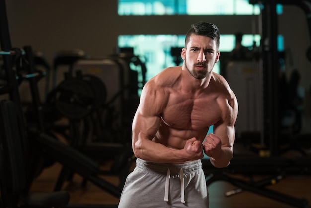 Jeune homme debout fort dans la salle de gym et muscles de la flexion Muscular Athletic Bodybuilder Fitness Model Posing After Exercises