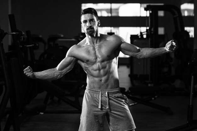 Jeune homme debout fort dans la salle de gym et muscles de la flexion Muscular Athletic Bodybuilder Fitness Model Posing After Exercises