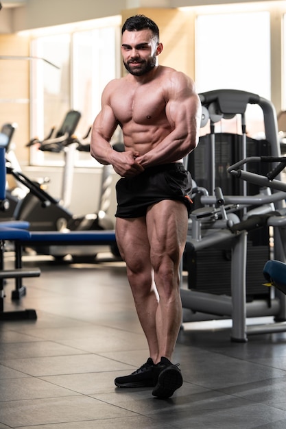 Jeune homme debout fort dans la salle de gym et muscles de la flexion Muscular Athletic Bodybuilder Fitness Model Posing After Exercises