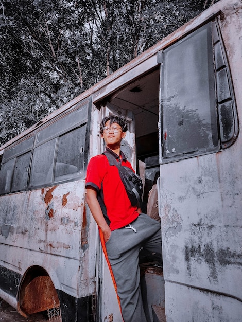 Photo un jeune homme debout près d'un bus abandonné