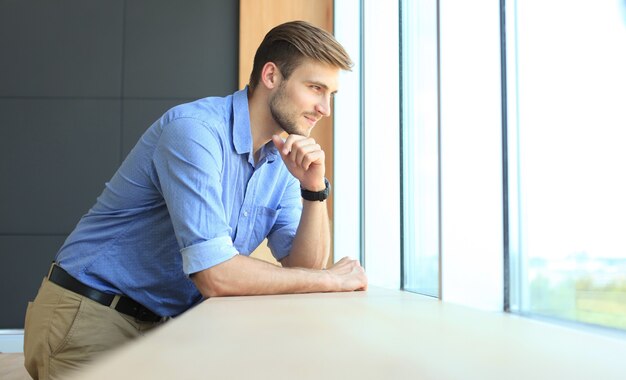 Jeune homme debout près de la fenêtre de son bureau en pensant à ses objectifs