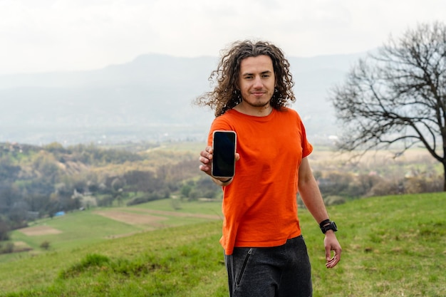 Jeune homme debout et tenant un téléphone portable sur la colline