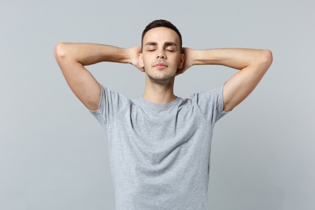 Jeune homme décontracté dans des vêtements décontractés gardant les yeux fermés, dormant les mains derrière la tête