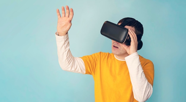 Jeune homme décontracté utilisant des lunettes VR touchant quelque chose d'invisible à l'espace de copie homme millénaire vivant une aventure de réalité virtuelle sur fond de studio bleu panorama réalité augmentée