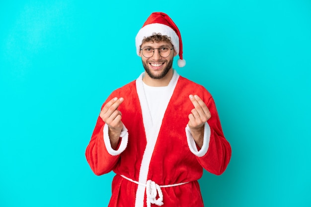 Jeune homme déguisé en Père Noël isolé sur fond bleu faisant un geste d'argent