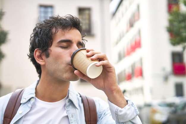 Un jeune homme démarre sa journée bien remplie avec un café à emporter rafraîchissant en se rendant au travail en ville