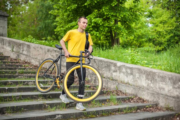 Un jeune homme descend les escaliers avec son vélo dans un parc public