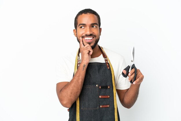 Jeune homme de design équatorien tenant des ciseaux isolé sur fond blanc en pensant à une idée tout en levant les yeux