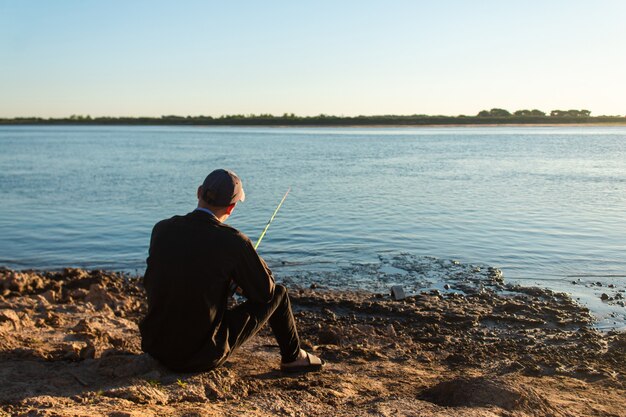 Jeune homme détente pêche assis sur le rivage de la rivière.