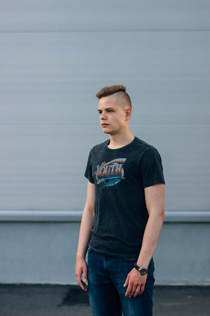 Un jeune homme détournant les yeux alors qu'il se tient contre le mur.