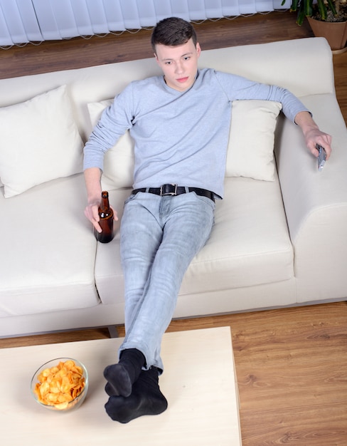 Jeune homme devant la télé et buvant de la bière à la maison.
