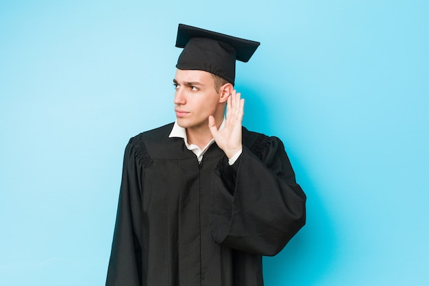 Jeune homme diplômé caucasien essayant d'écouter un potin.