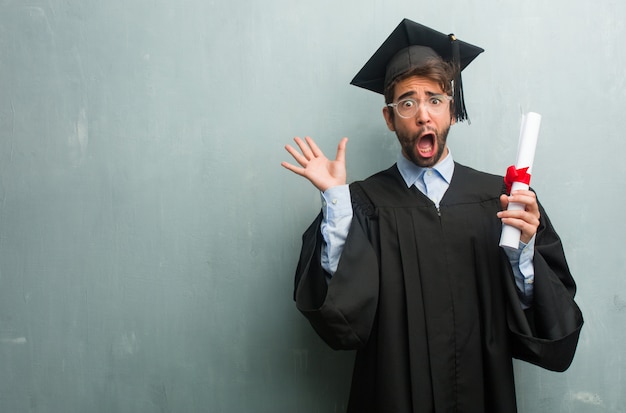 Jeune homme diplômé contre un mur de grunge avec un espace de copie fou et désespéré