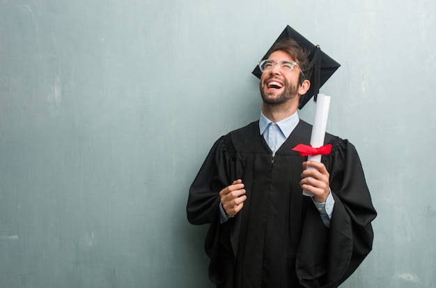 Jeune homme diplômé contre un mur de grunge avec un espace copie rire et s&#39;amuser