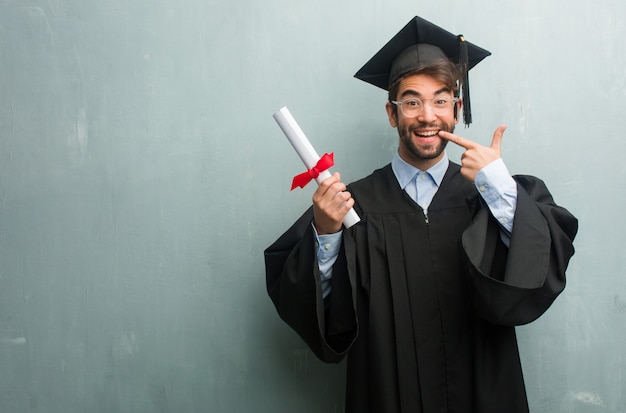 Jeune homme diplômé contre un mur de grunge avec un espace de copie sourit