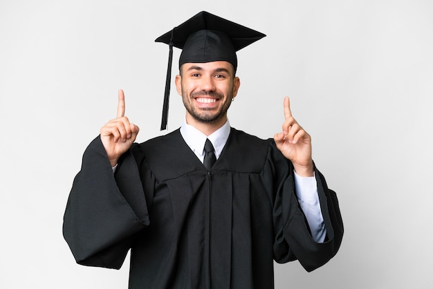 Jeune homme diplômé universitaire sur fond blanc isolé pointant vers le haut une excellente idée