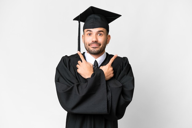Jeune homme diplômé universitaire sur fond blanc isolé pointant vers les latéraux ayant des doutes