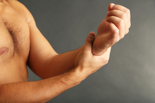 Jeune homme avec douleur à la main sur fond gris