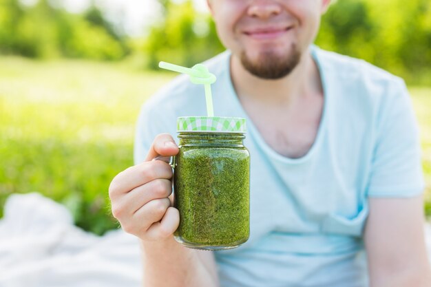 Jeune homme drôle détient un smoothie de désintoxication avec de la paille. Concept de mode de vie sain, de personnes et de nourriture.