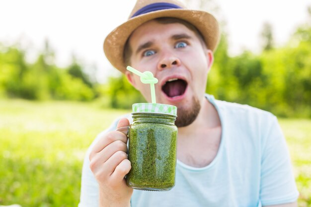 Jeune homme drôle détient un smoothie de désintoxication avec de la paille. Concept de mode de vie sain, de personnes et de nourriture.