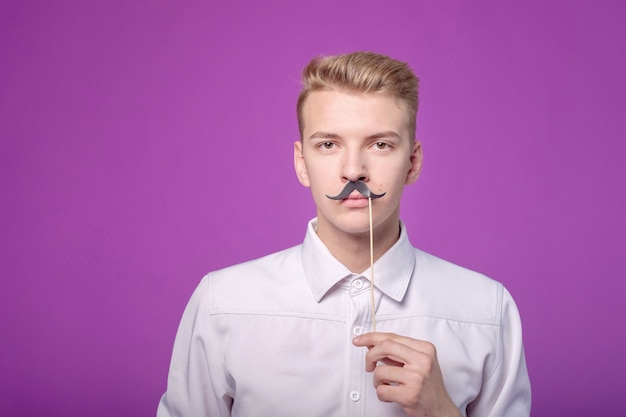 Jeune homme drôle avec la moustache de papier sur le fond