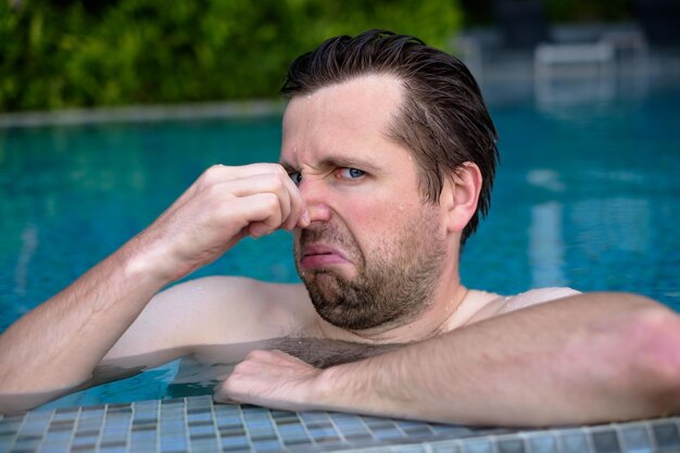 Un jeune homme avec du dégoût sur le visage pince le nez quelque chose pue une très mauvaise odeur dans la piscine à cause du chlorure