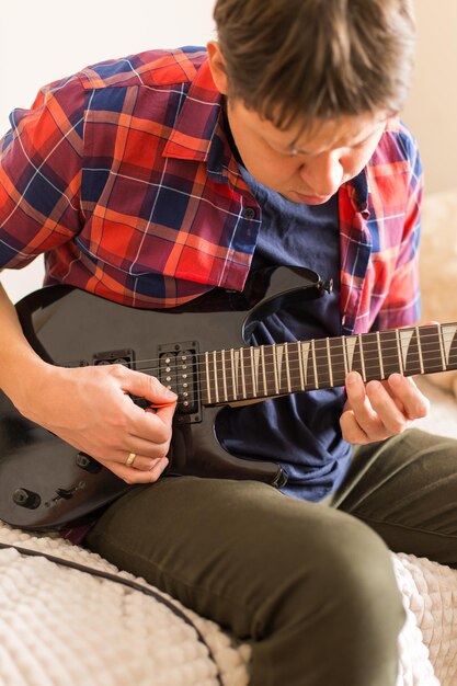 Jeune homme du millénaire, gars jouant de la guitare électrique. Rester à la maison, activité à la maison, cours d'apprentissage