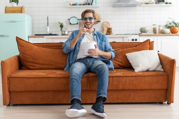 Jeune homme avec du pop-corn dans les mains devant la télévision à la maison.