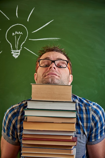 Jeune homme échevelé tenant une pile de livres.