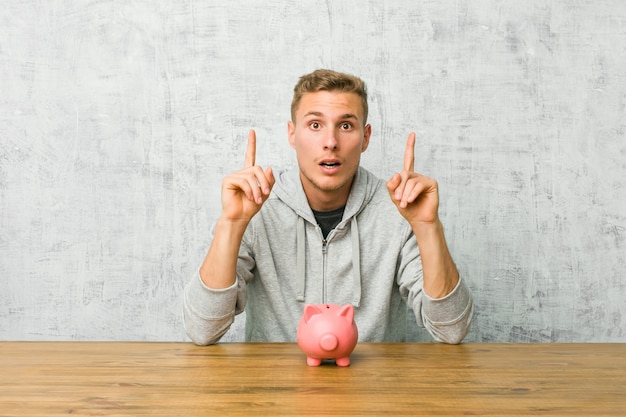 Jeune homme, économiser de l'argent avec une tirelire pointant à l'envers avec la bouche ouverte.