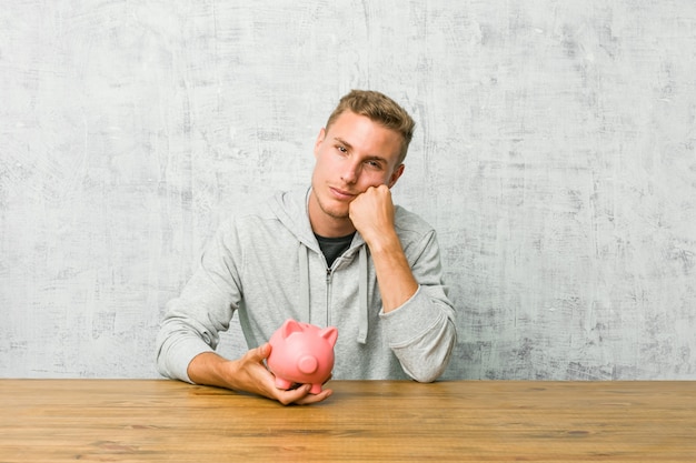 Jeune homme, économiser de l'argent avec une tirelire qui se sent triste et pensive, en regardant l'espace copie.