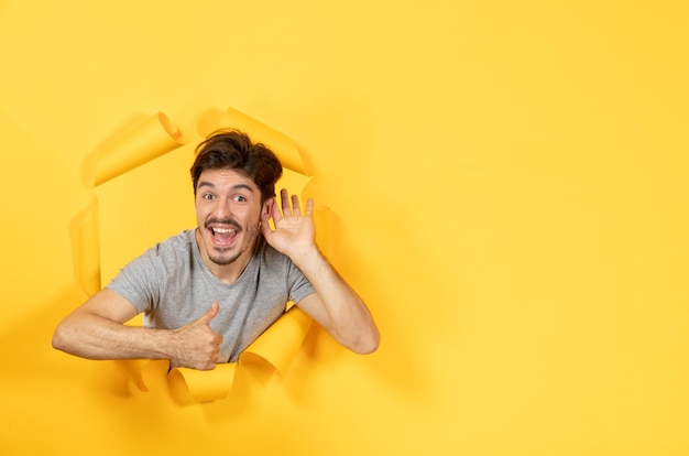 Jeune homme écoutant et regardant de la vente de gars à l'intérieur de fond de papier jaune déchiré