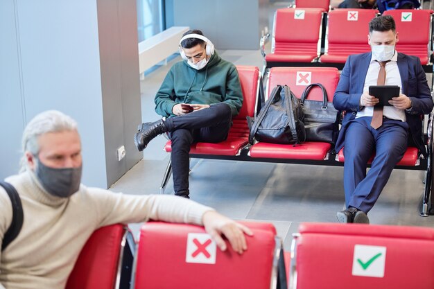 Photo jeune homme avec des écouteurs écoutant de la musique et faisant défiler un smartphone pendant qu'un homme d'affaires utilise une tablette numérique dans le salon