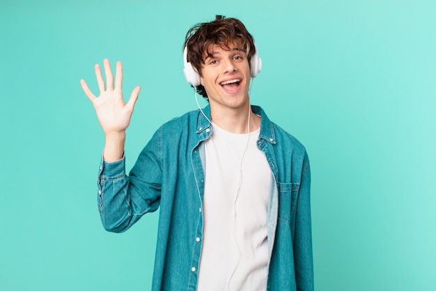 Jeune homme avec des écouteurs souriant joyeusement, agitant la main, vous accueillant et vous saluant