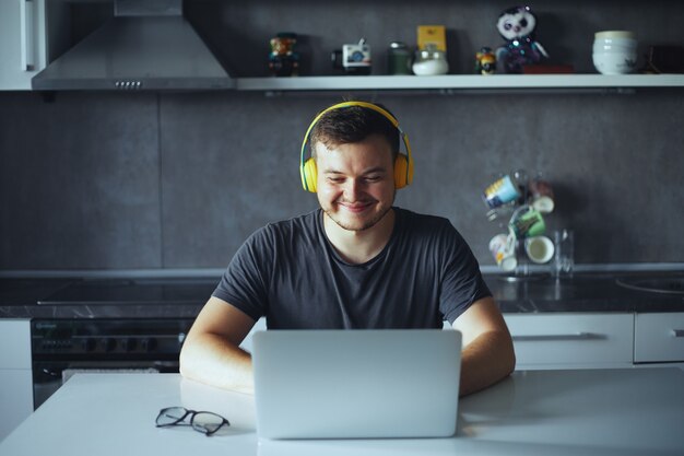 Jeune homme avec des écouteurs souriant tout en regardant un ordinateur portable écoutant de la musique