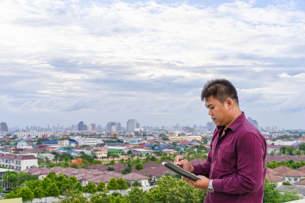 jeune homme écrivant des notes debout dans un fond de vue de la ville