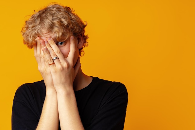 Jeune homme effrayé couvrant le visage avec les mains sur fond jaune