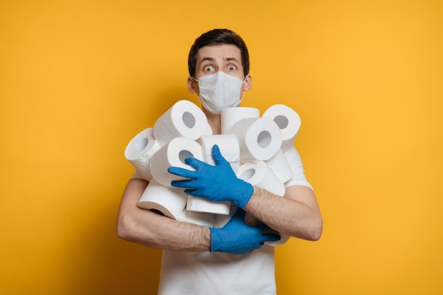 Jeune homme effrayé tenant de nombreux rouleaux de papier toilette