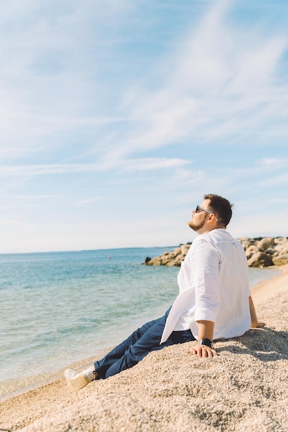Jeune homme élégant assis sur la plage de la mer en profitant de la vue concept de vacances d'été espace de copie