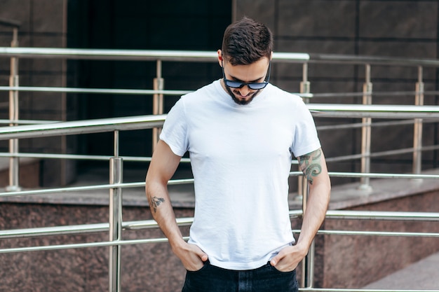 Un jeune homme élégant avec une barbe dans un t-shirt blanc et des lunettes de soleil