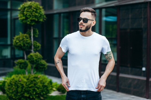 Un jeune homme élégant avec une barbe dans un t-shirt blanc et des lunettes de soleil