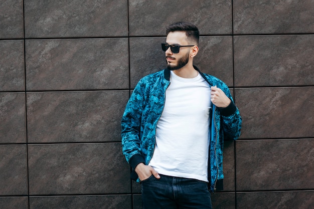 Un jeune homme élégant avec une barbe dans un t-shirt blanc et des lunettes de soleil