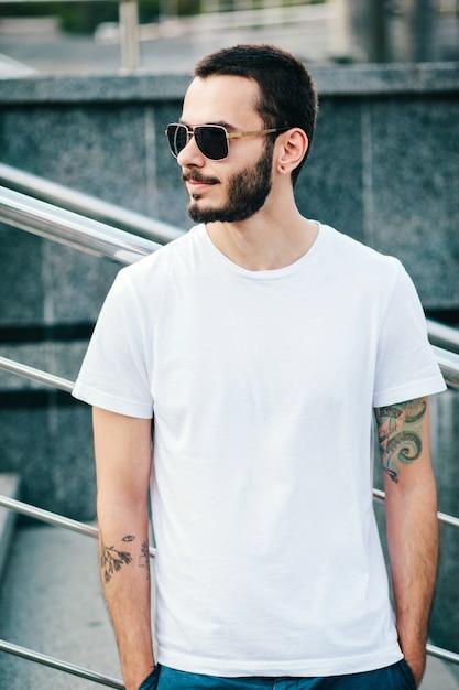 Un jeune homme élégant avec une barbe dans un T-shirt blanc et des lunettes