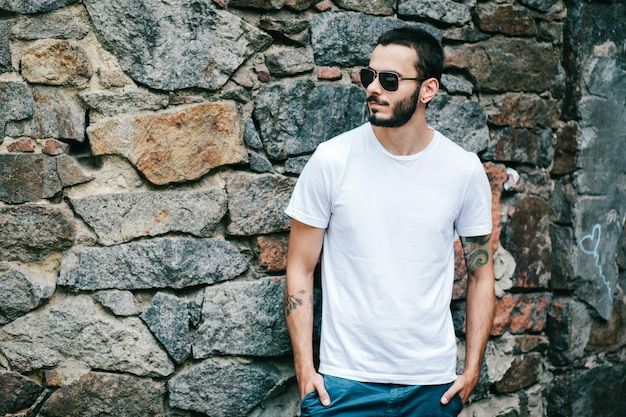 Un jeune homme élégant avec une barbe dans un T-shirt blanc et des lunettes