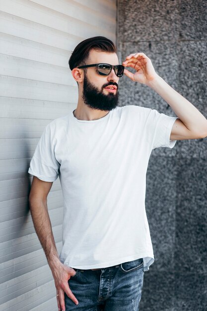 Un jeune homme élégant avec une barbe dans un Tshirt blanc et des lunettes Street photo