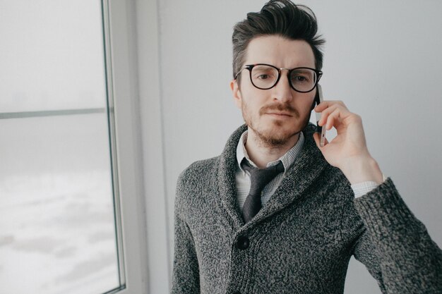 Photo un jeune homme élégant avec une barbe et des lunettes dans une chemise et un cardigan gris contre un mur gris