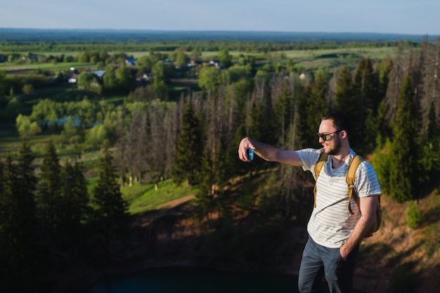 Jeune homme élégant avec une barbe portant des lunettes de soleil prenant selfie sur la falaise du canyon