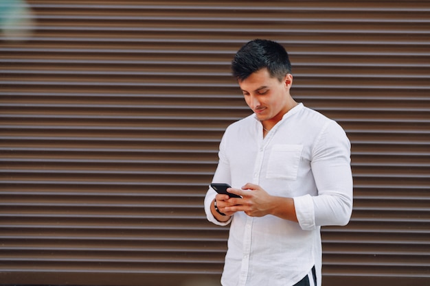 Jeune homme élégant en chemise en tapant sur le téléphone sur fond simple